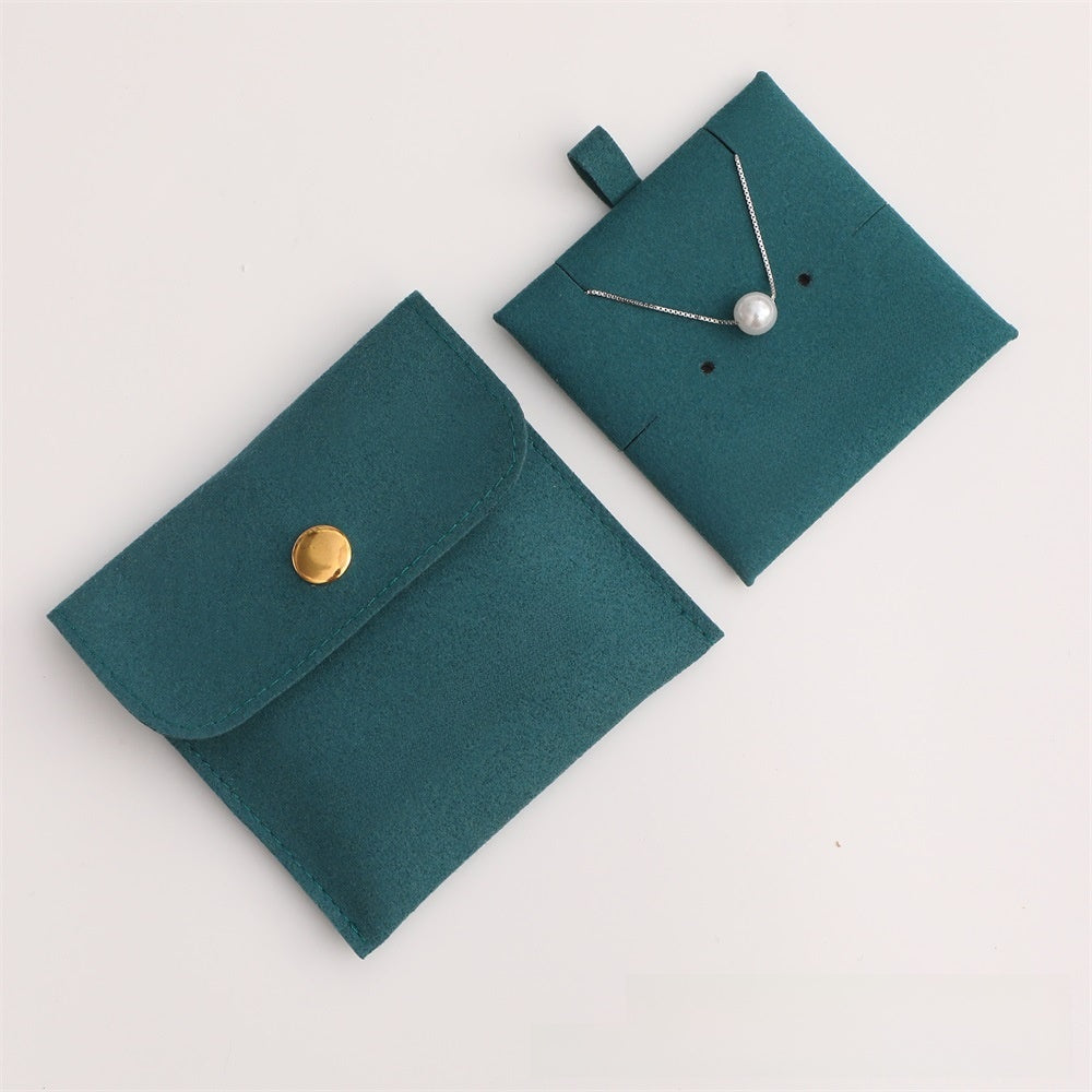 Teal jewelry pouch with a gold button and necklace on a light gray background
