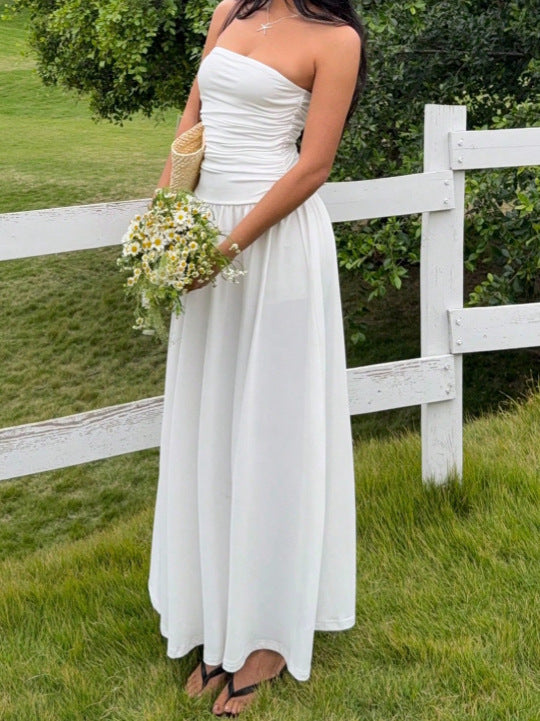 Woman in a white strapless dress holding flowers in a grassy area with a white fence.