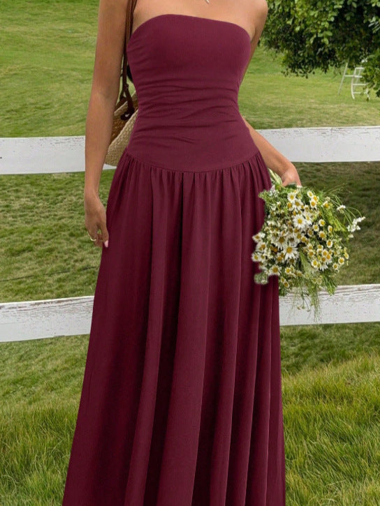 Woman in a burgundy strapless dress holding flowers outdoors.