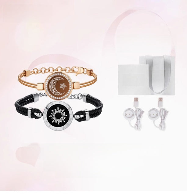 Two bracelets with moon and sun designs, a white box, and charging cables on a light pink background.