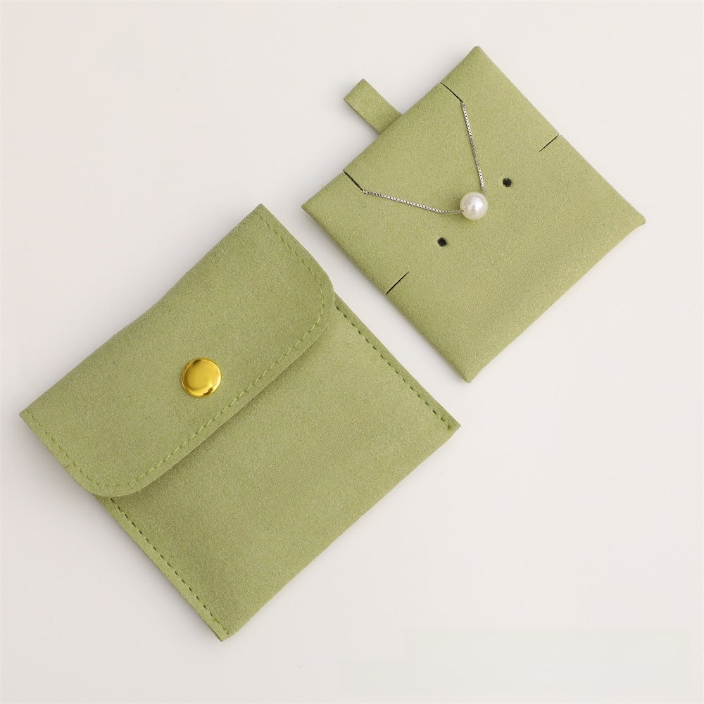 Green jewelry pouch with a gold button and a necklace on a light gray background