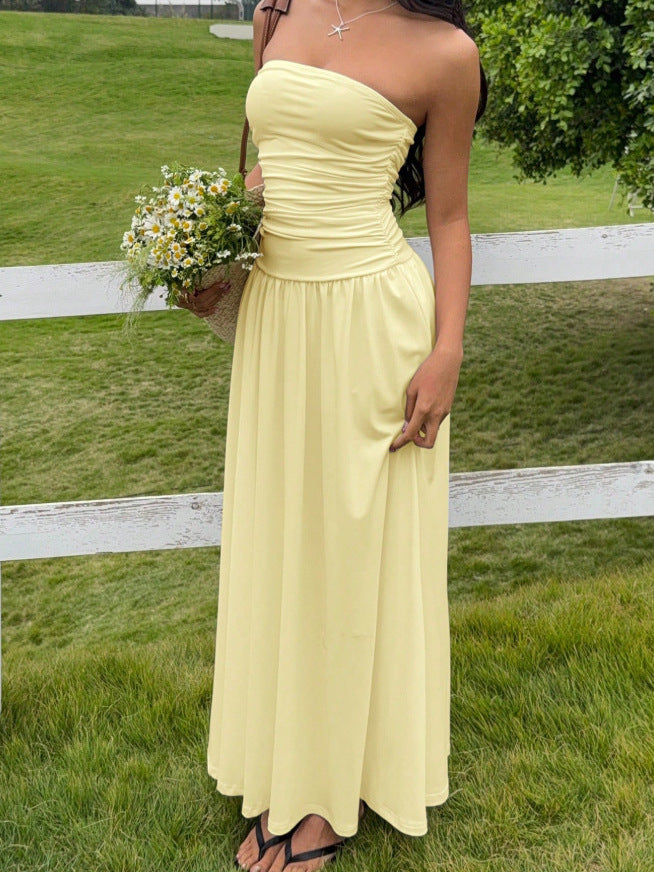 Woman in a yellow strapless dress holding flowers in a grassy outdoor setting